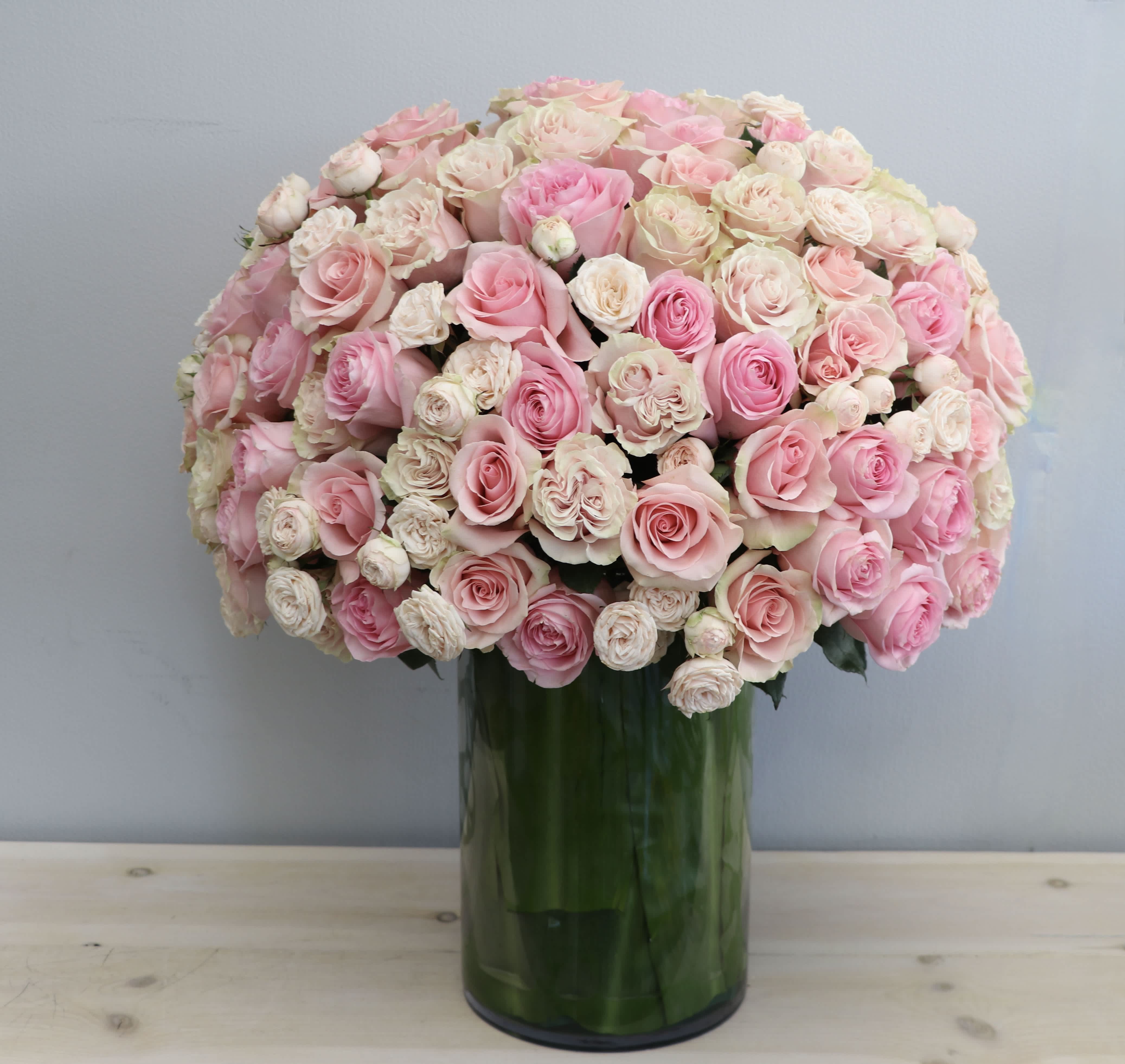 Large dome of pink and ivory roses in a tall glass cylinder vase