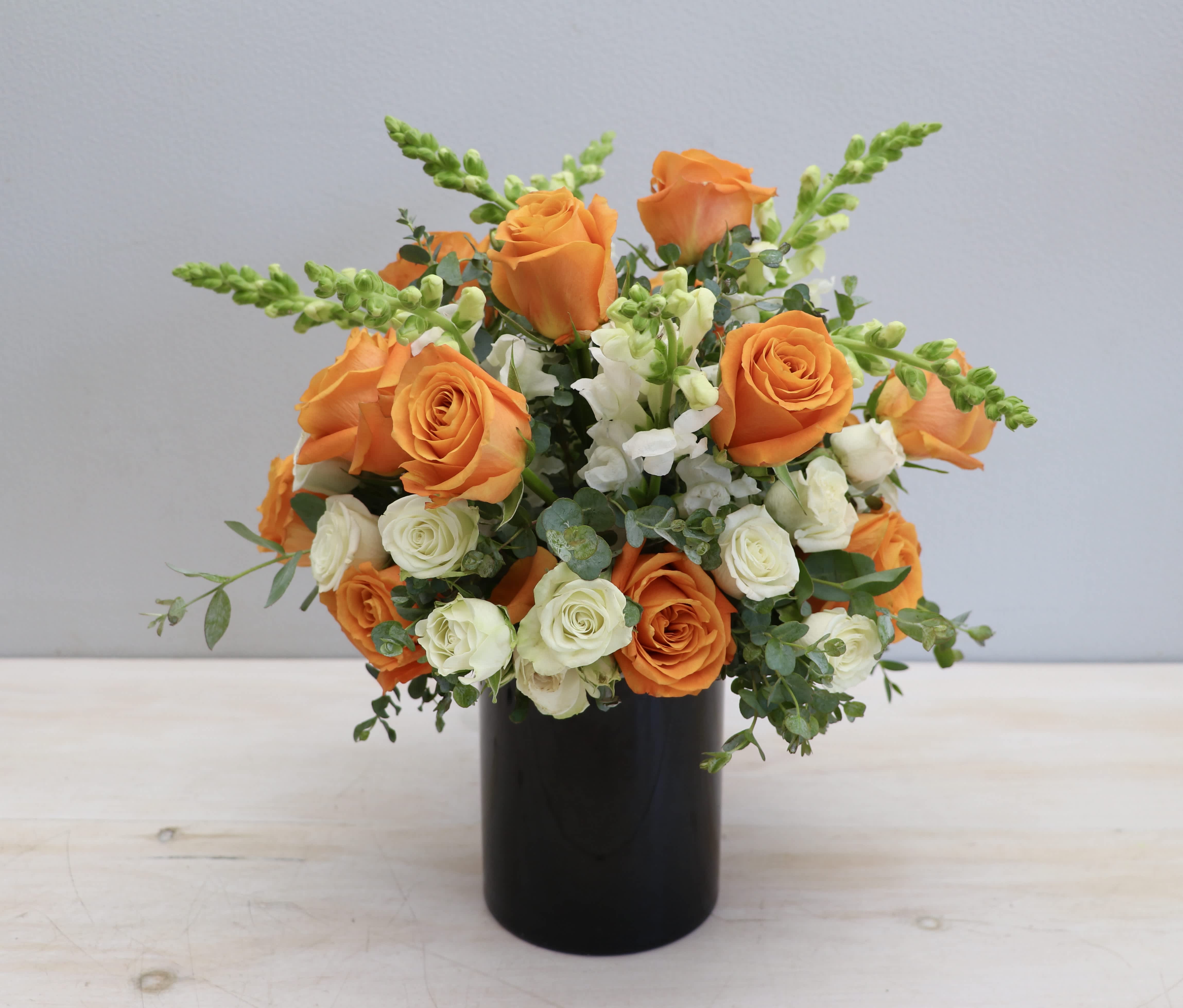 Orange and cream roses with white snapdragons in a black cylinder vase