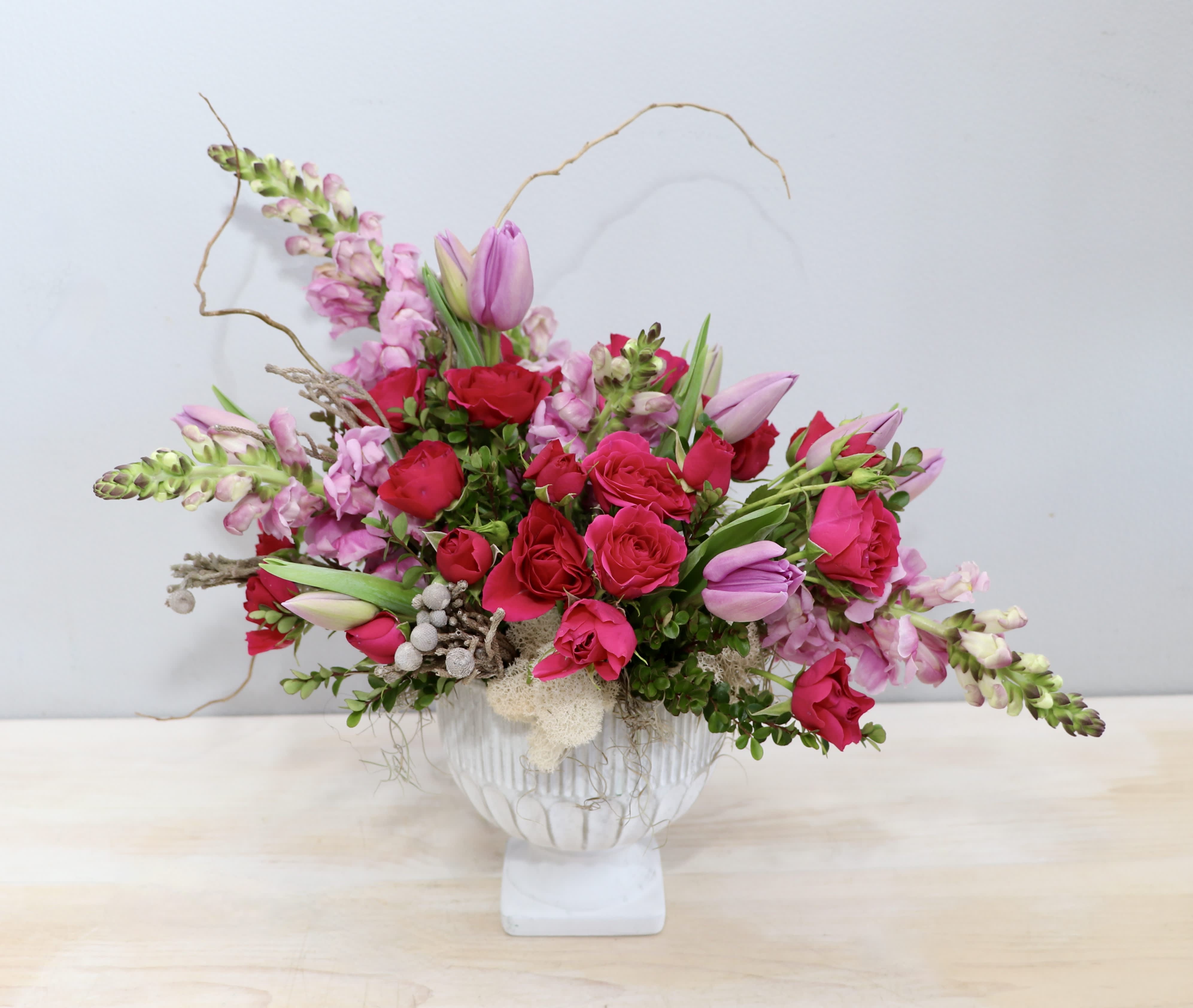 Asymmetrical arrangement of bright pink roses and tulips in a white pedestal vase