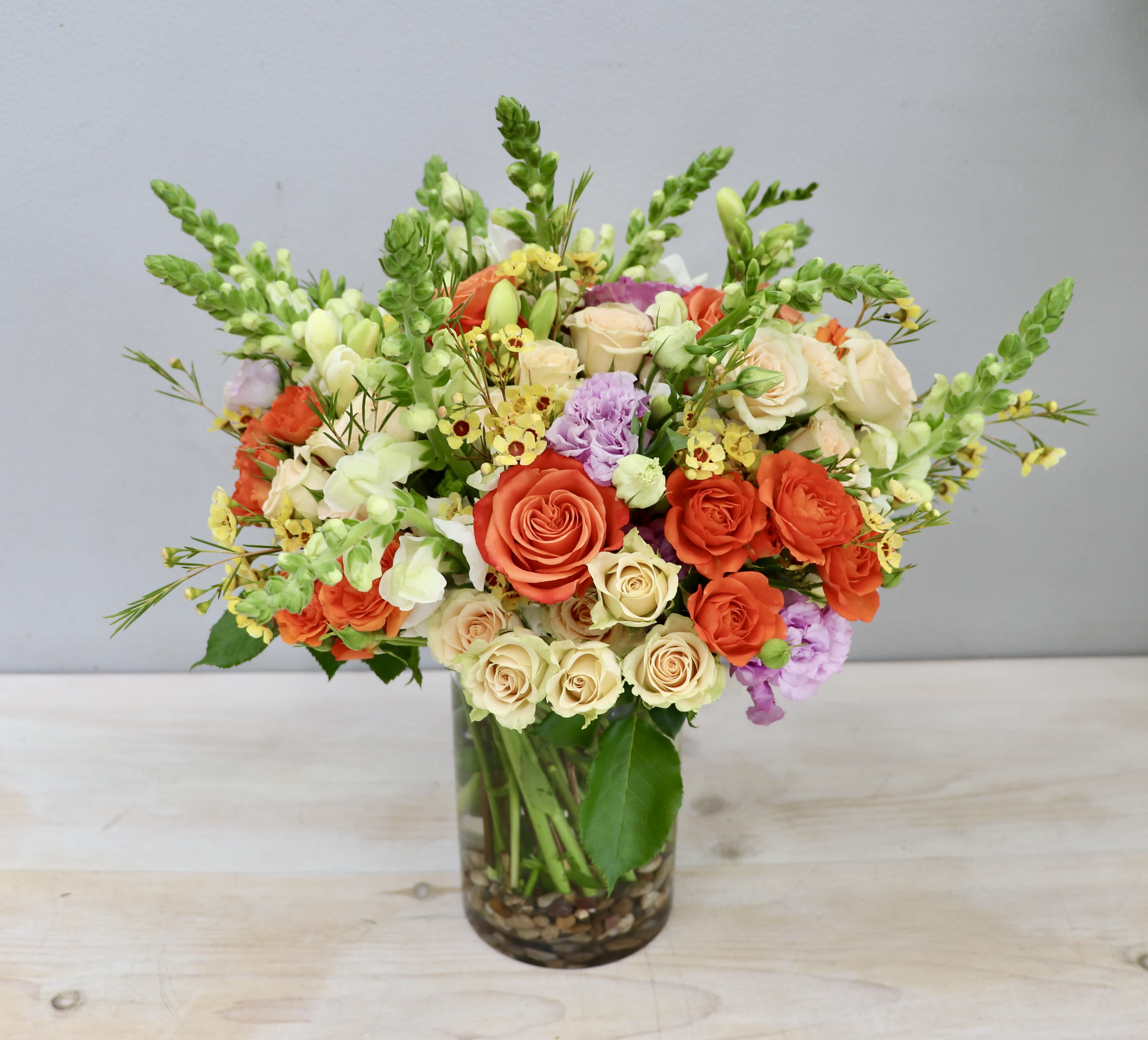 Vase arrangement of orange and cream roses with snapdragons and touches of yellow and lavender flowers