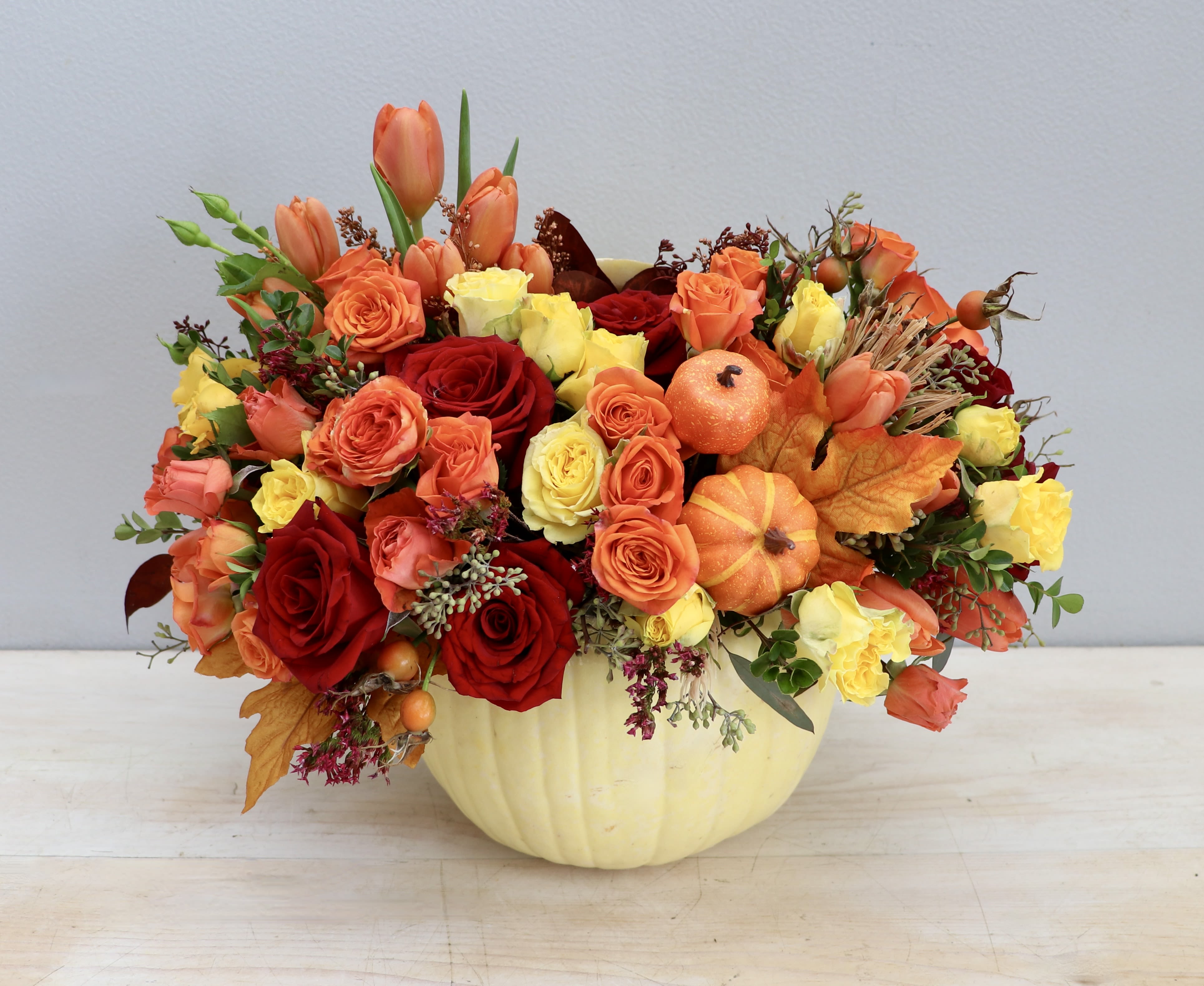 Fall arrangement of orange and yellow roses and tulips with mini pumpkins in a white pumpkin container