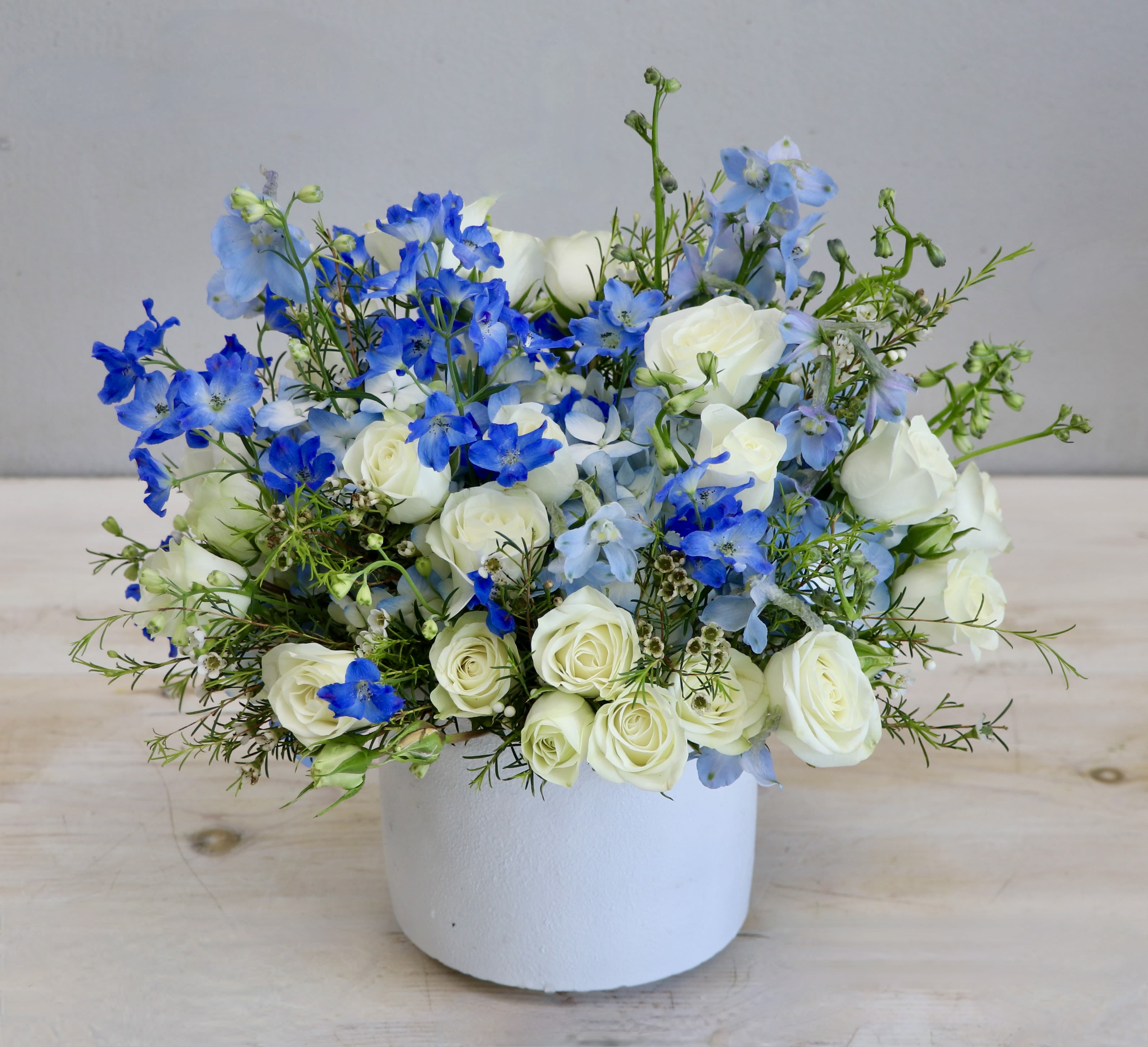 Low arrangement of white roses and blue delphinium in a white pot