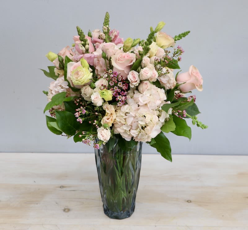 Tall arrangement of pale pink roses and hydrangeas with accent blooms in a faceted glass vase