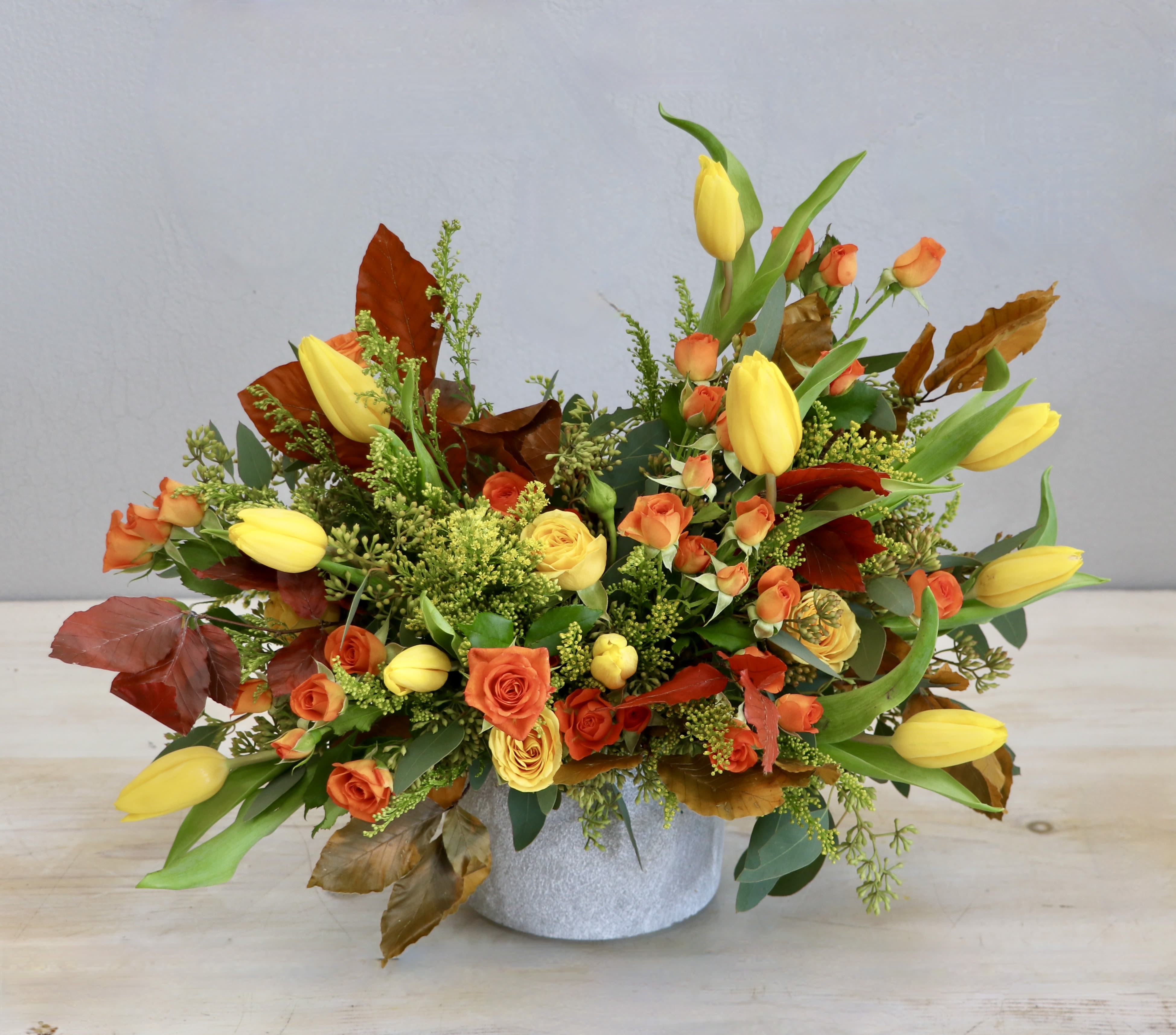 Low arrangement of yellow tulips and orange roses in a round white container