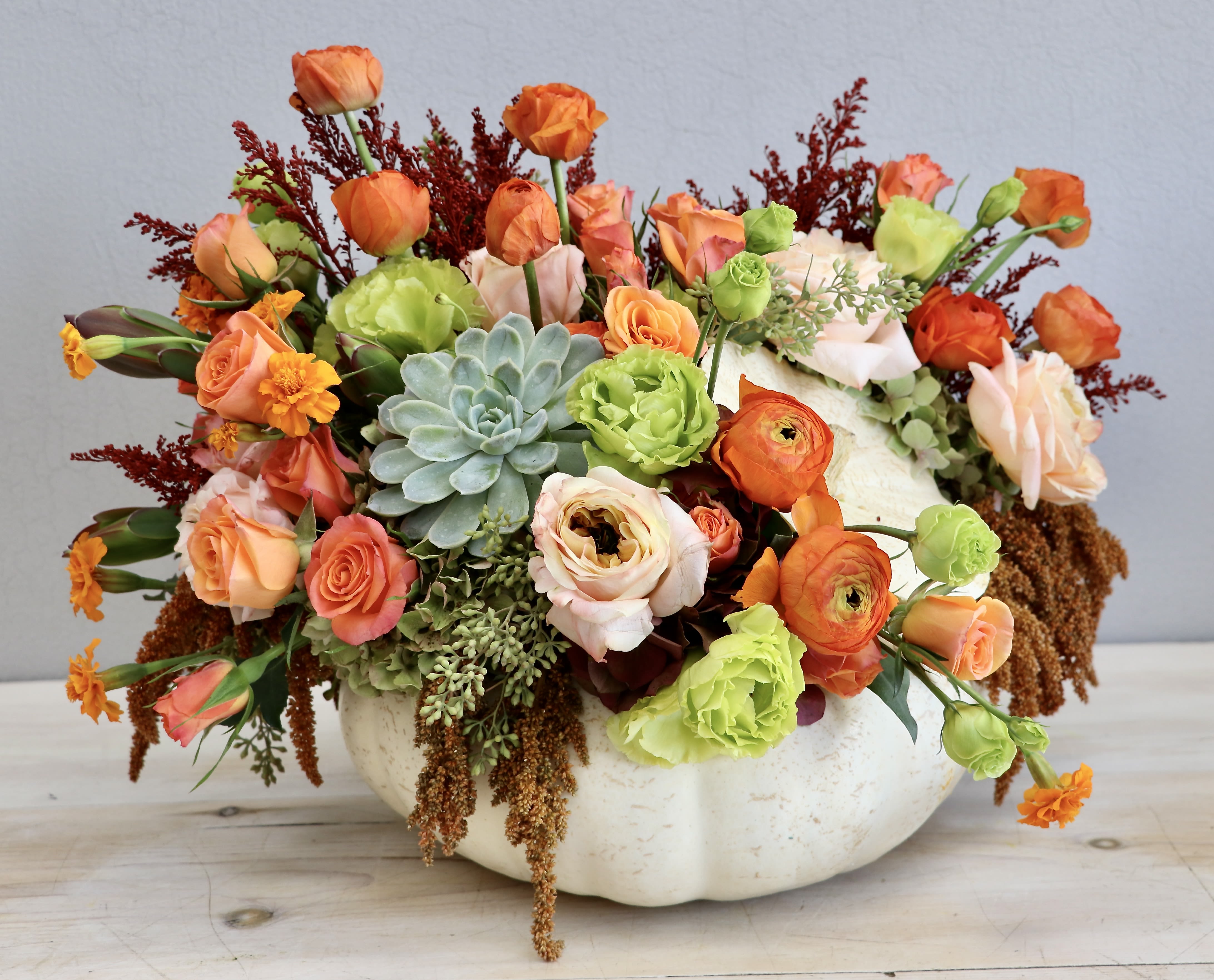 Low pumpkin arrangement with orange and peach roses, ranunculus, green flowers, and a central succulent
