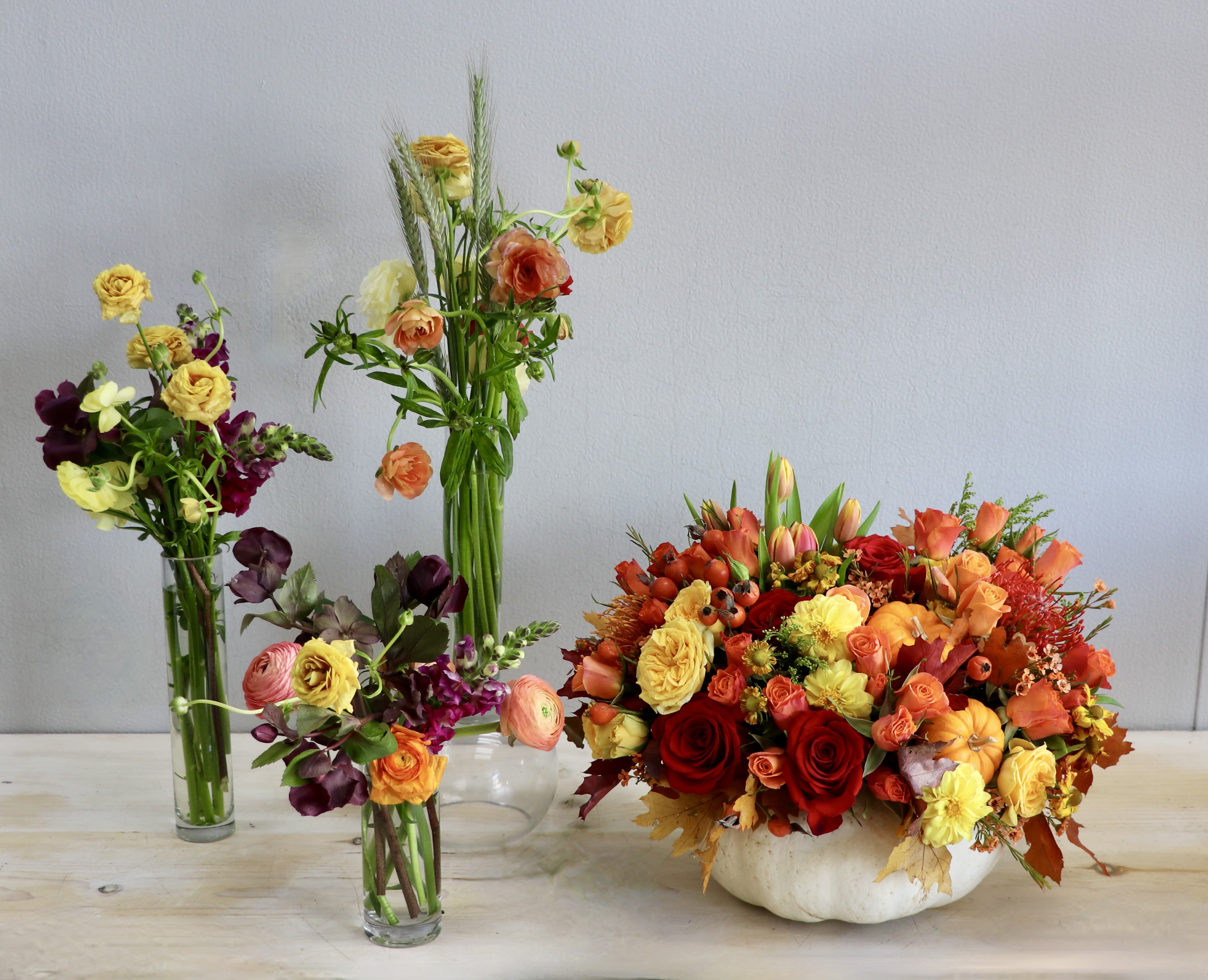 Autumn centerpiece of orange and yellow flowers in a white pumpkin with three smaller mixed bud vases.