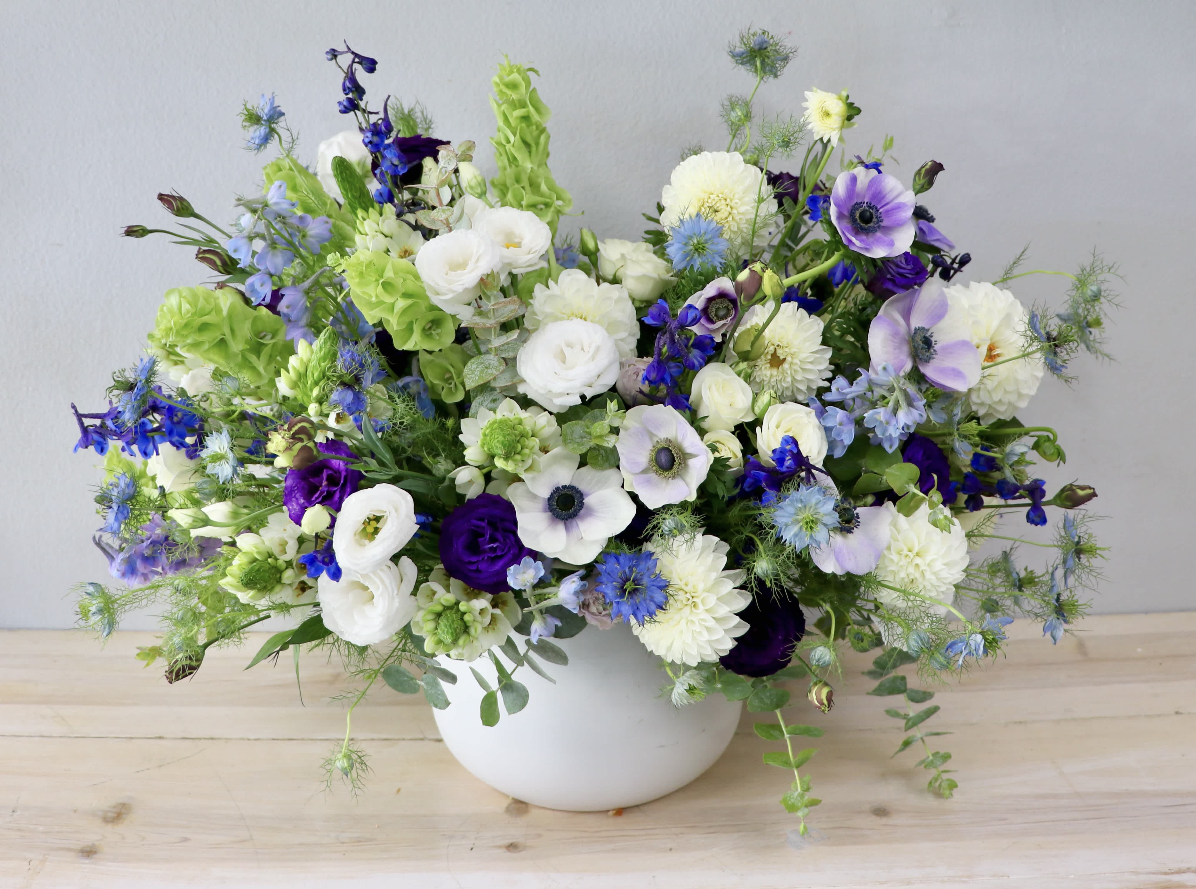 Mixed white, blue, and purple flowers in a white bowl vase