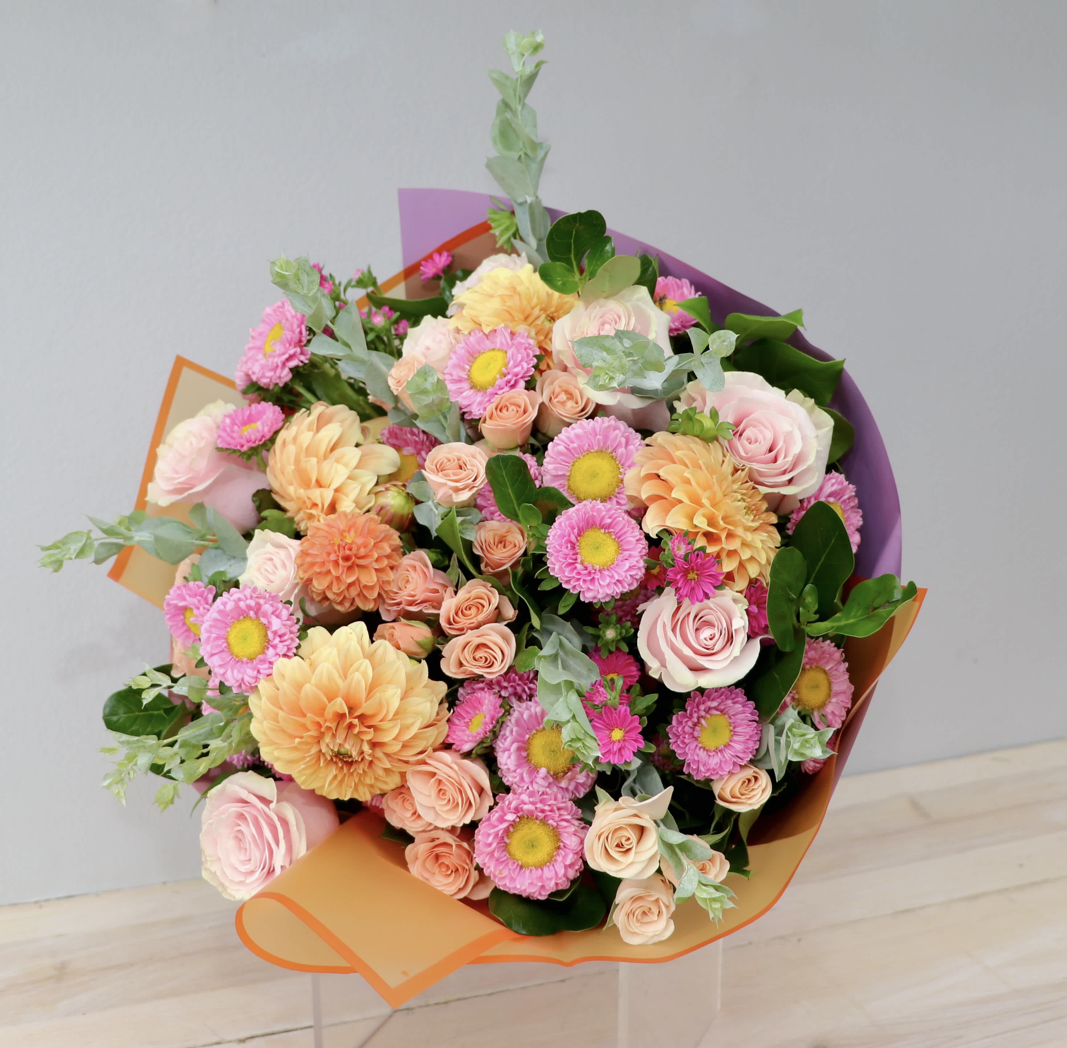 Bouquet of pink and peach flowers wrapped in orange and purple paper