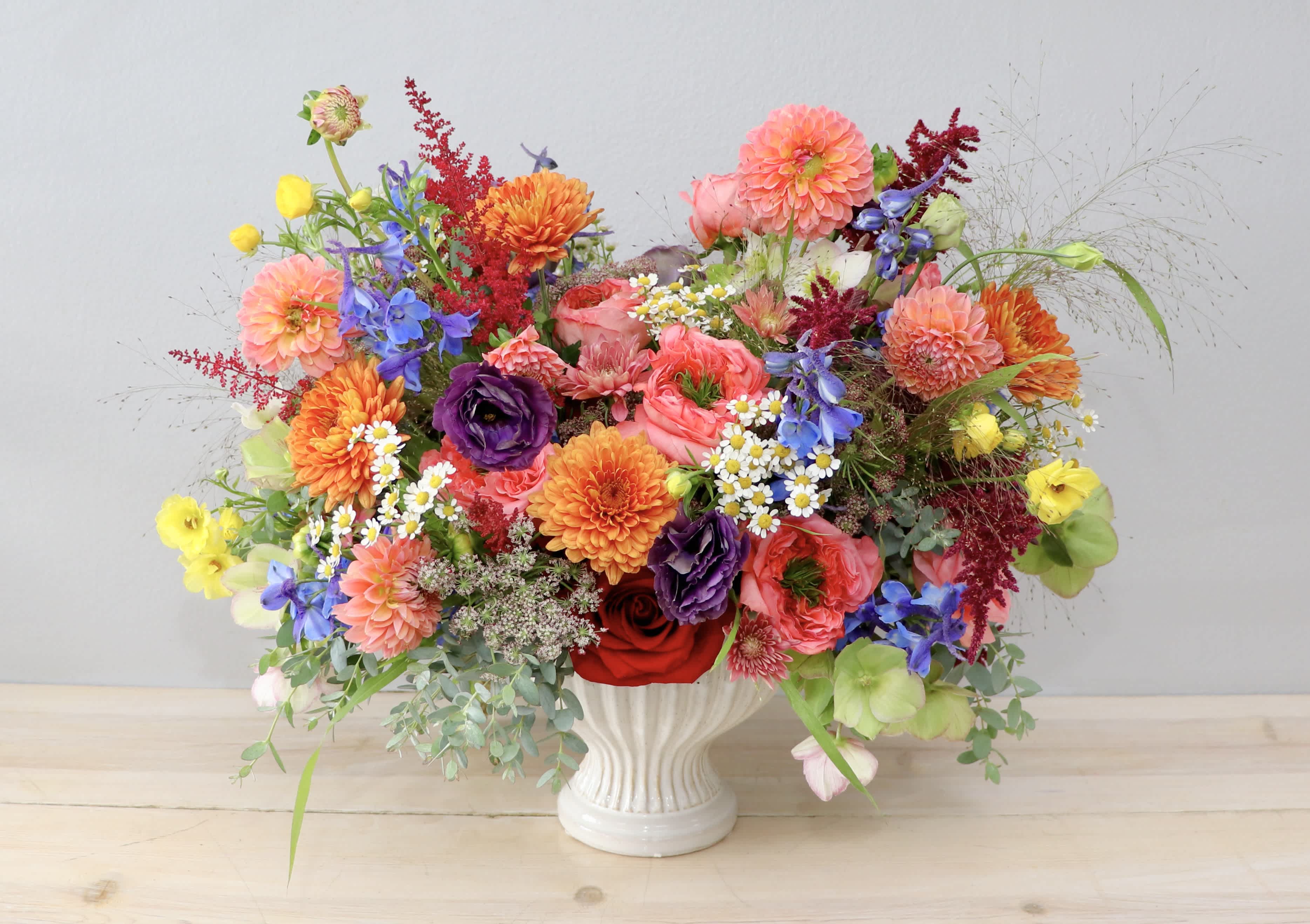 Colorful mixed bouquet in a white vase with dahlias, roses, and blue flowers