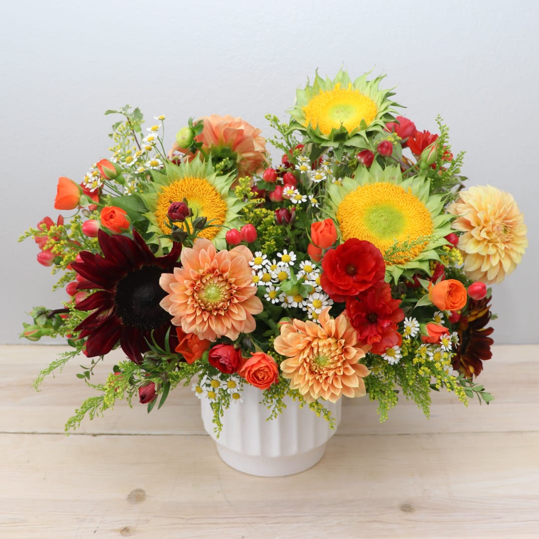 Mixed bouquet with sunflowers, dahlias, and roses in a white vase
