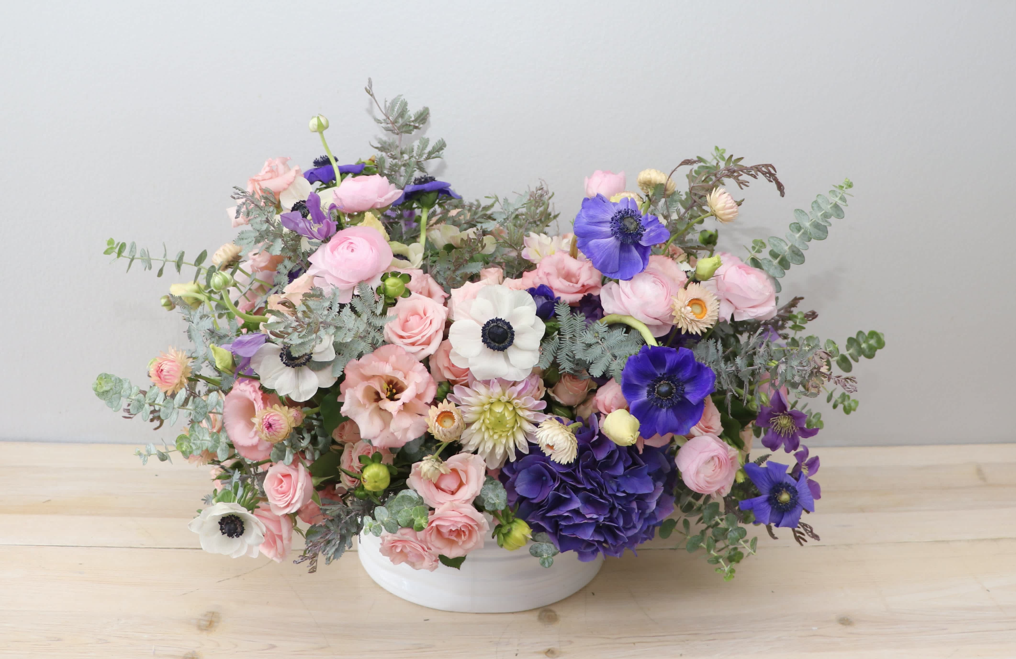 Pink and purple mixed flower arrangement in a white bowl vase