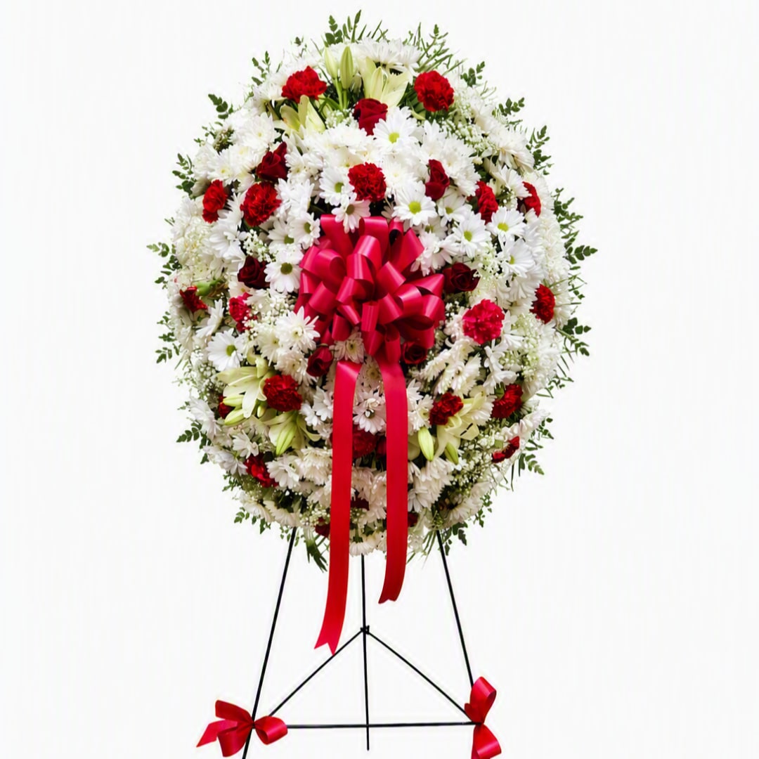 Standing floral wreath of white and red flowers with a pink ribbon bow
