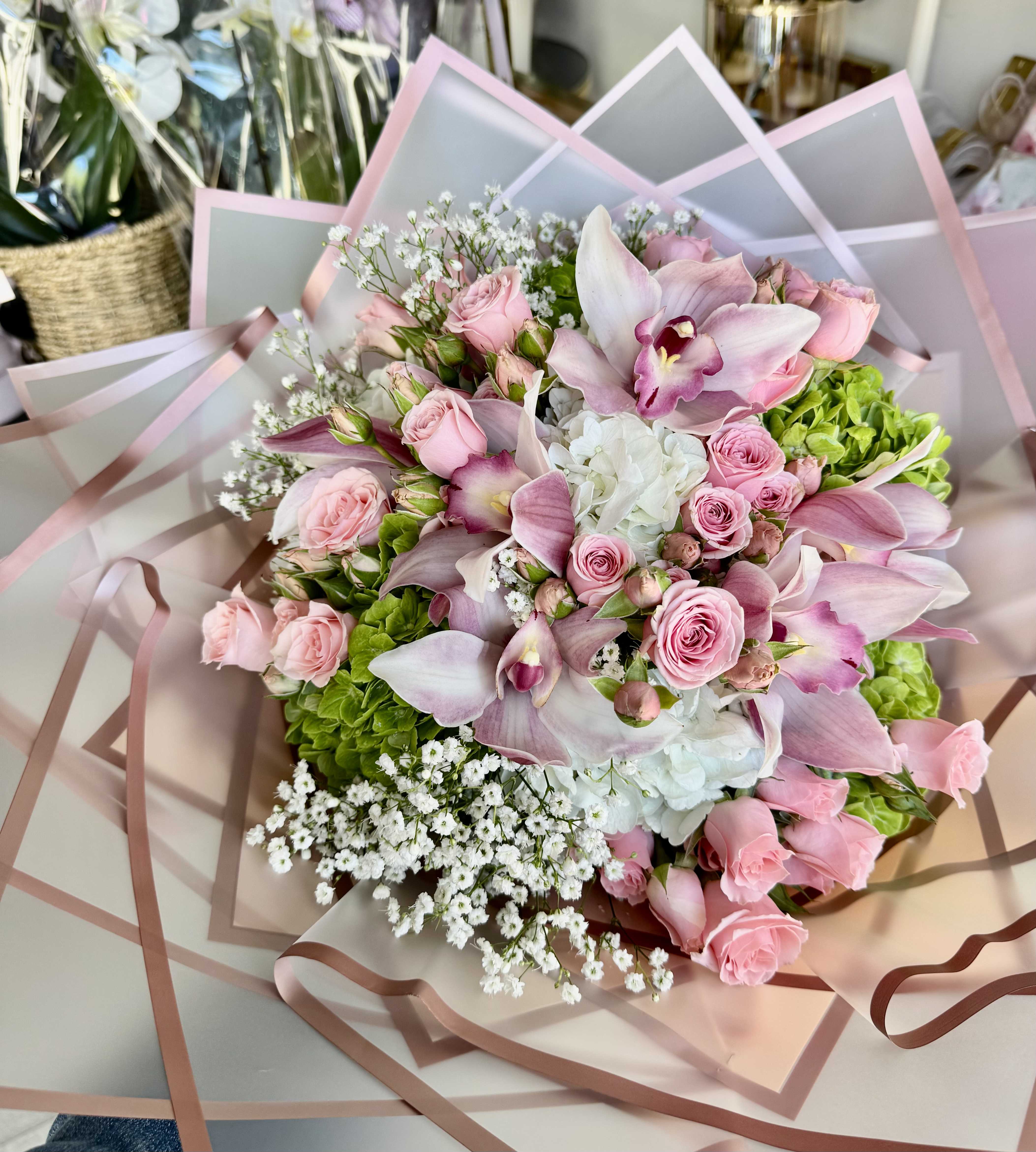 Pink roses and orchids arranged with white filler flowers in pastel wrap