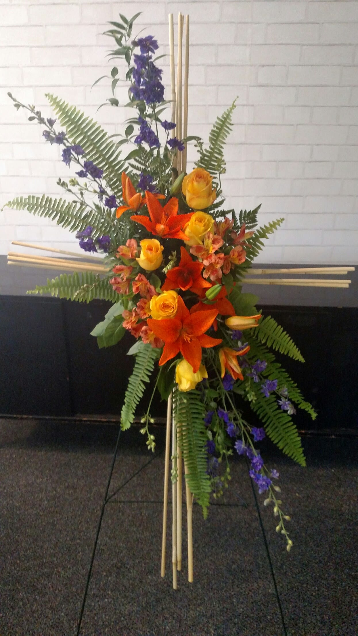 Tall floral standing arrangement with orange lilies, yellow roses, and purple flowers