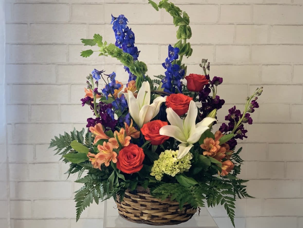 Basket arrangement with red roses, white lilies, and blue delphinium