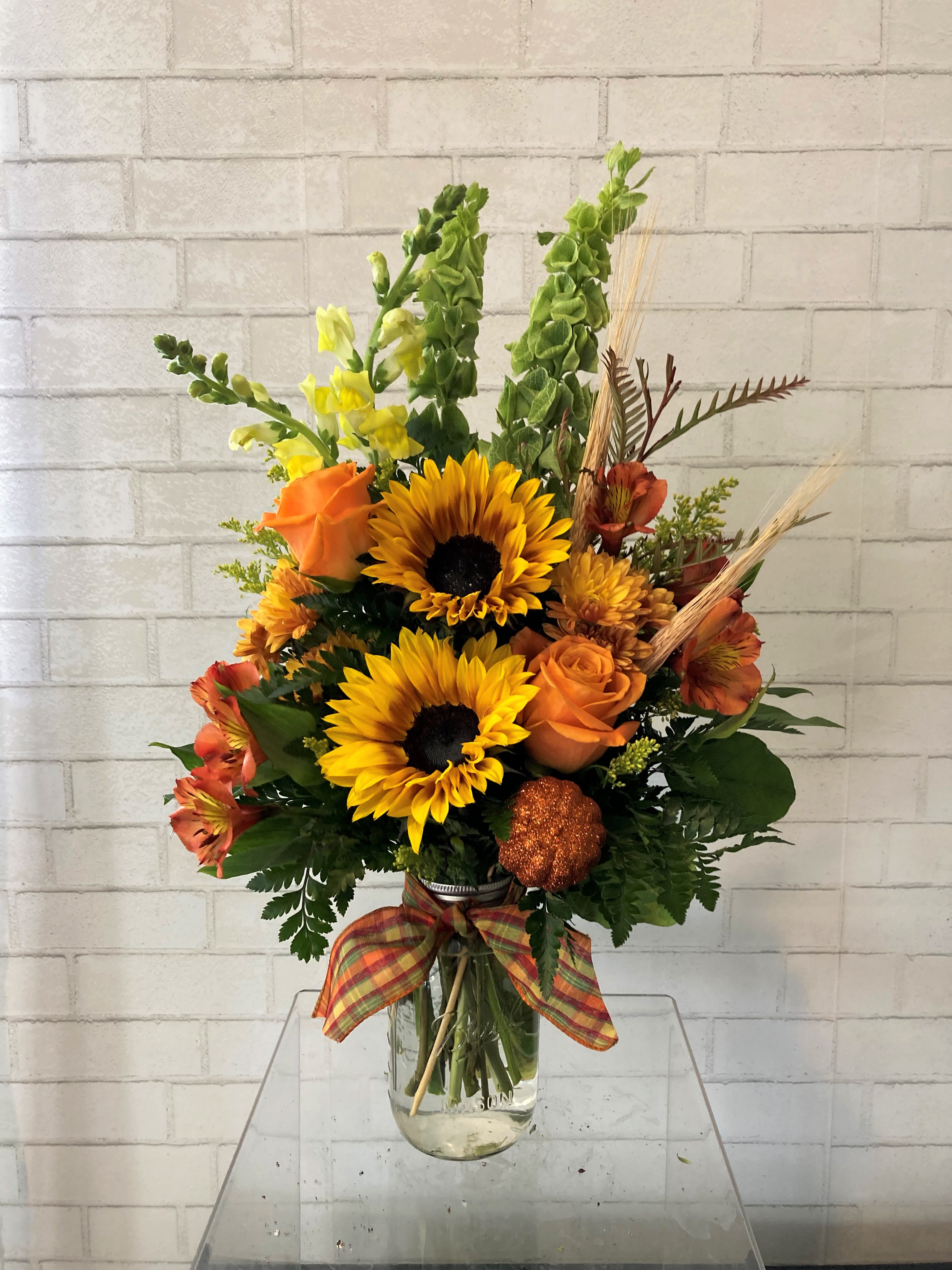 Autumn bouquet with sunflowers, orange roses, and a glass vase.