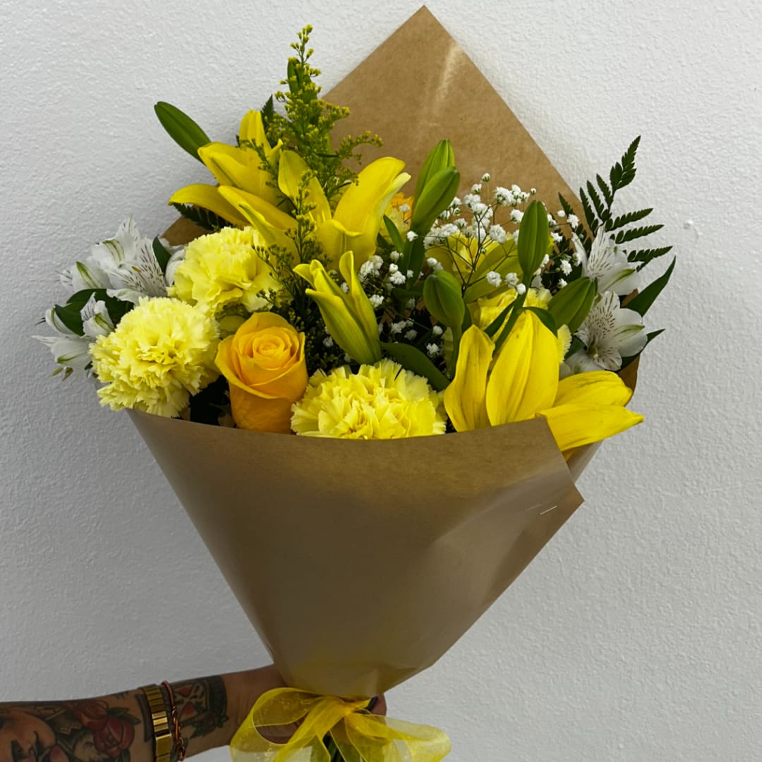 Yellow bouquet with lilies, roses, carnations, and white filler flowers in brown paper