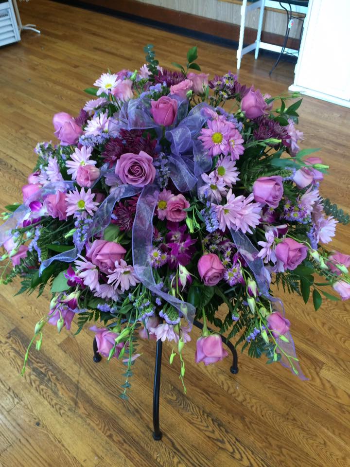 Pink and purple floral arrangement on a black stand with ribbon
