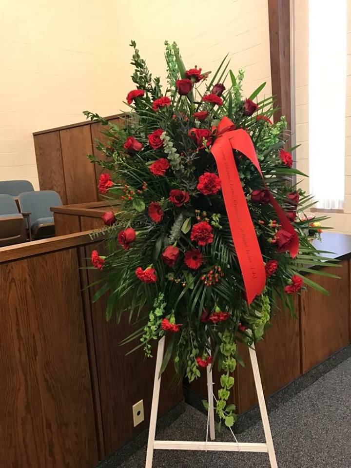 Standing red floral wreath on an easel with a ribbon