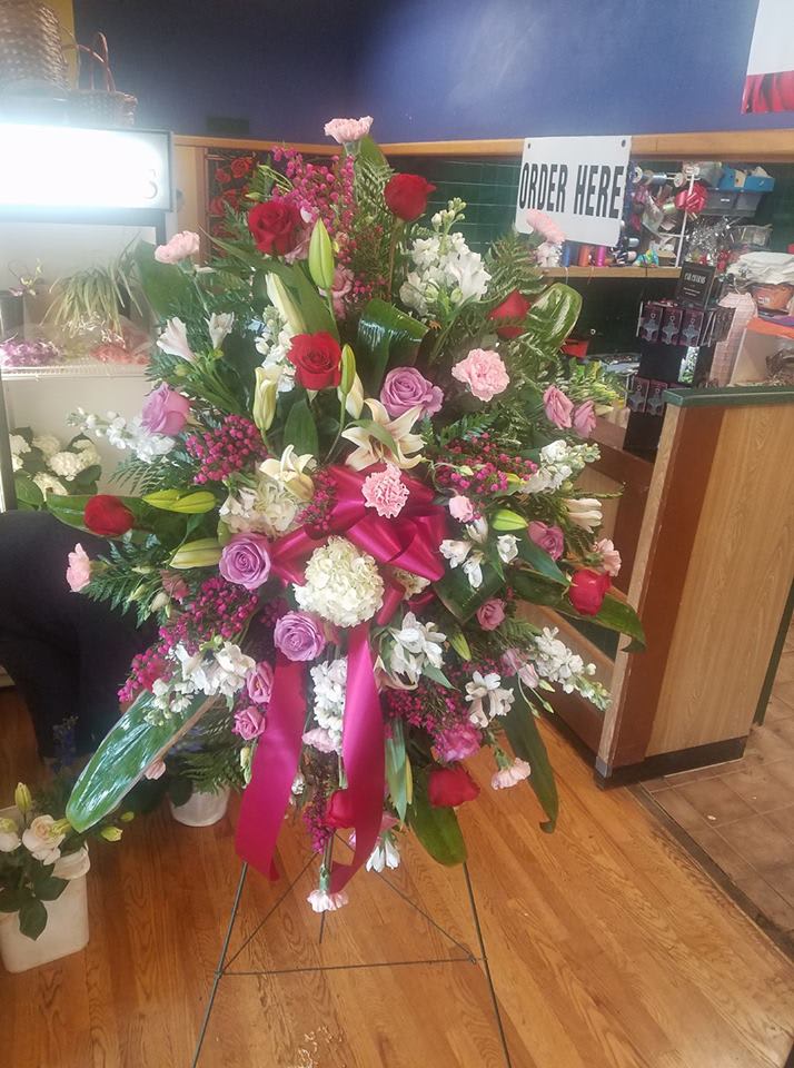 Large standing floral spray with roses, lilies, and pink ribbon