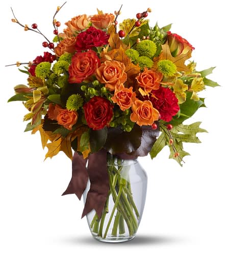 Autumn arrangement of orange roses, red carnations, green mums and fall leaves in a clear glass vase