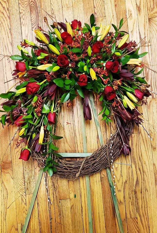 Heart-shaped wreath with red roses and yellow lilies on a wooden background