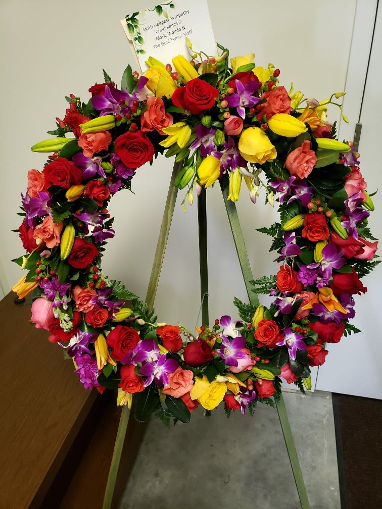 Colorful floral wreath on a stand with a sympathy card