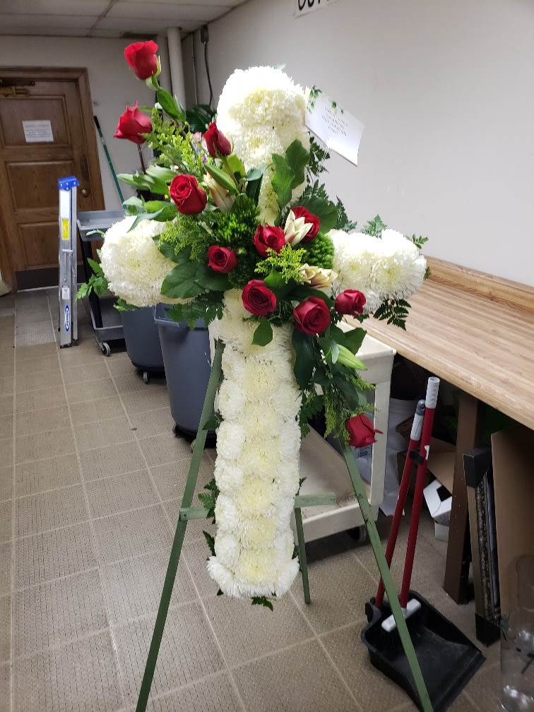 Standing floral cross with white blooms and red roses on an easel