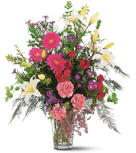 Mixed bouquet with pink gerbera daisies, red roses, white lilies, and carnations in a glass vase