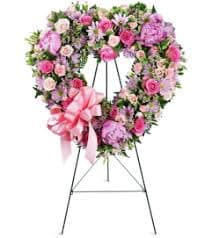 Heart-shaped pink and lavender floral wreath on an easel with a ribbon bow