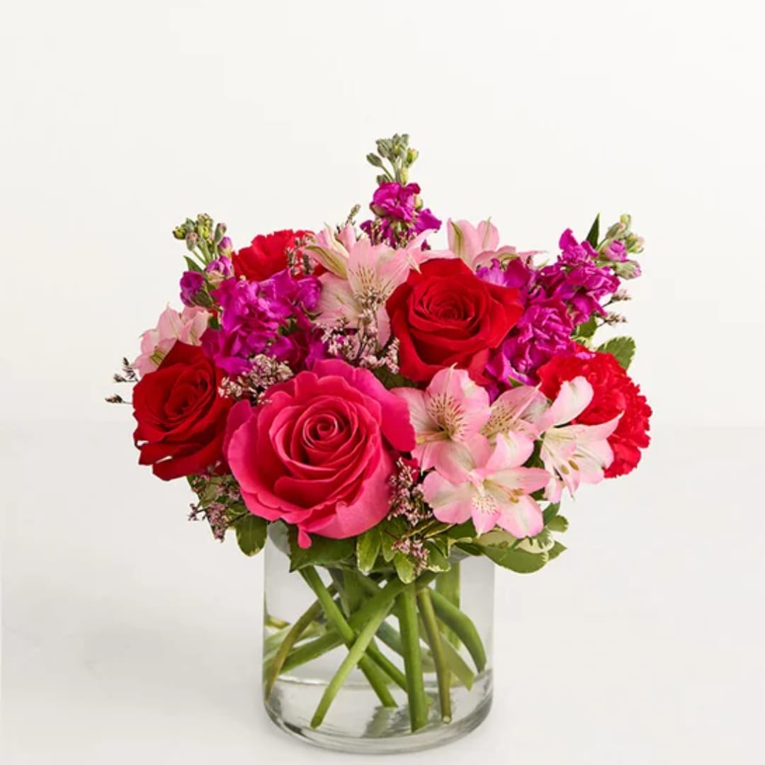 Bouquet of red and pink roses with pale pink lilies in a clear glass vase