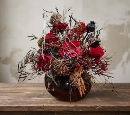 Red roses in a dark vase with dried accents and seed pods