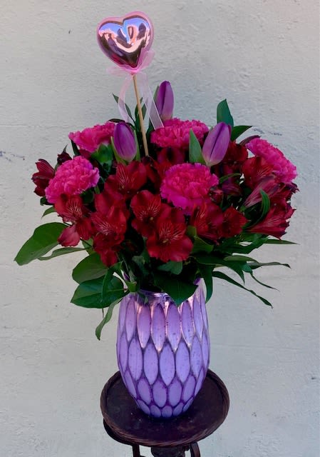 Bouquet of red and pink flowers in a purple vase with a heart balloon