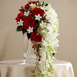 The FTD Here Comes the Bride Bouquet - The FTD® Here Comes the Bride™ Bouquet makes a dramatic presentation perfect for the bride that likes to hold everyone's attention. White dendrobium orchids cascade from a compact bouquet of red roses white stephanotis red hypericum berries green hydrangea and lush greens. Accented with rhinestone spray pics and dangling teardrop glass crystal stems this incredible bouquet is beautifully presented in a silver metallic bouquet holder.