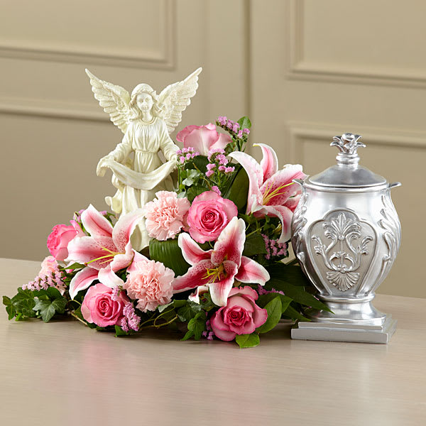 Pink lilies and roses arranged beside an angel figurine and silver urn