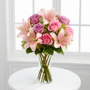 Pink lilies and roses arranged in a clear glass vase