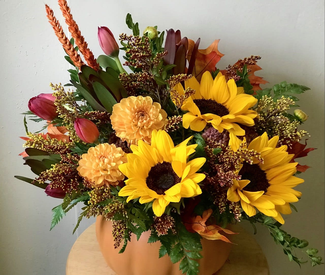 Autumn bouquet with sunflowers, tulips, and orange blooms in a pumpkin-colored vase.