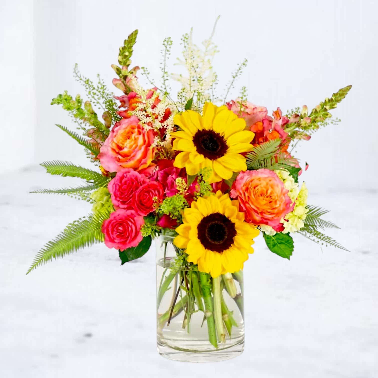 Bright mixed bouquet of sunflowers and roses in a clear glass vase