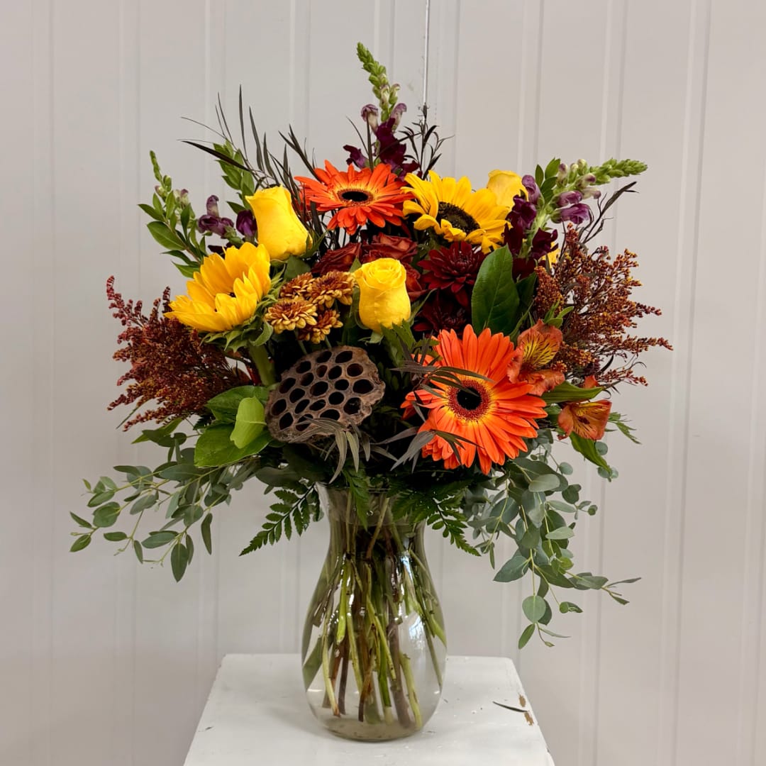 Mixed bouquet of sunflowers, gerbera daisies, and roses in a glass vase