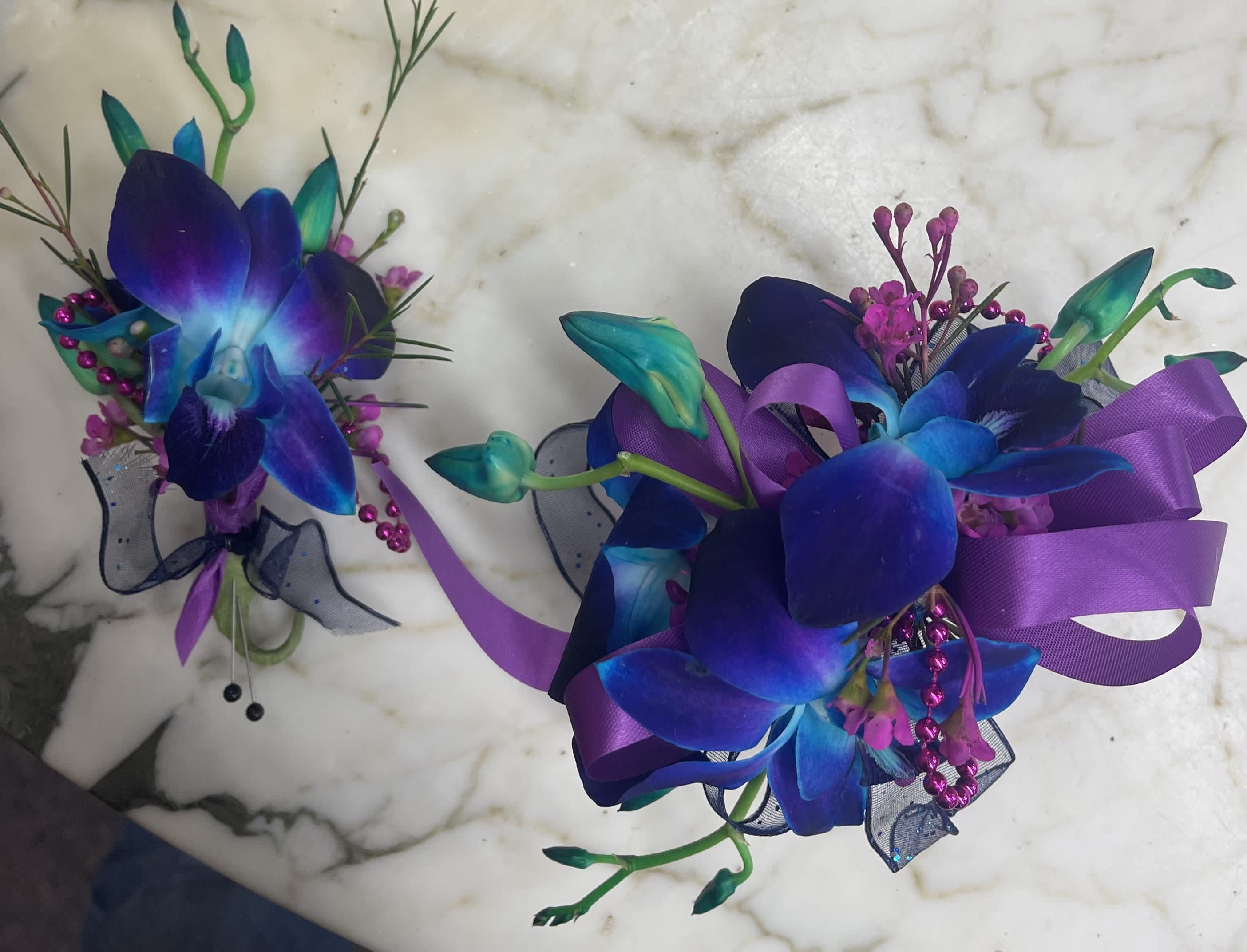 Two purple and blue orchid corsages with ribbon accents