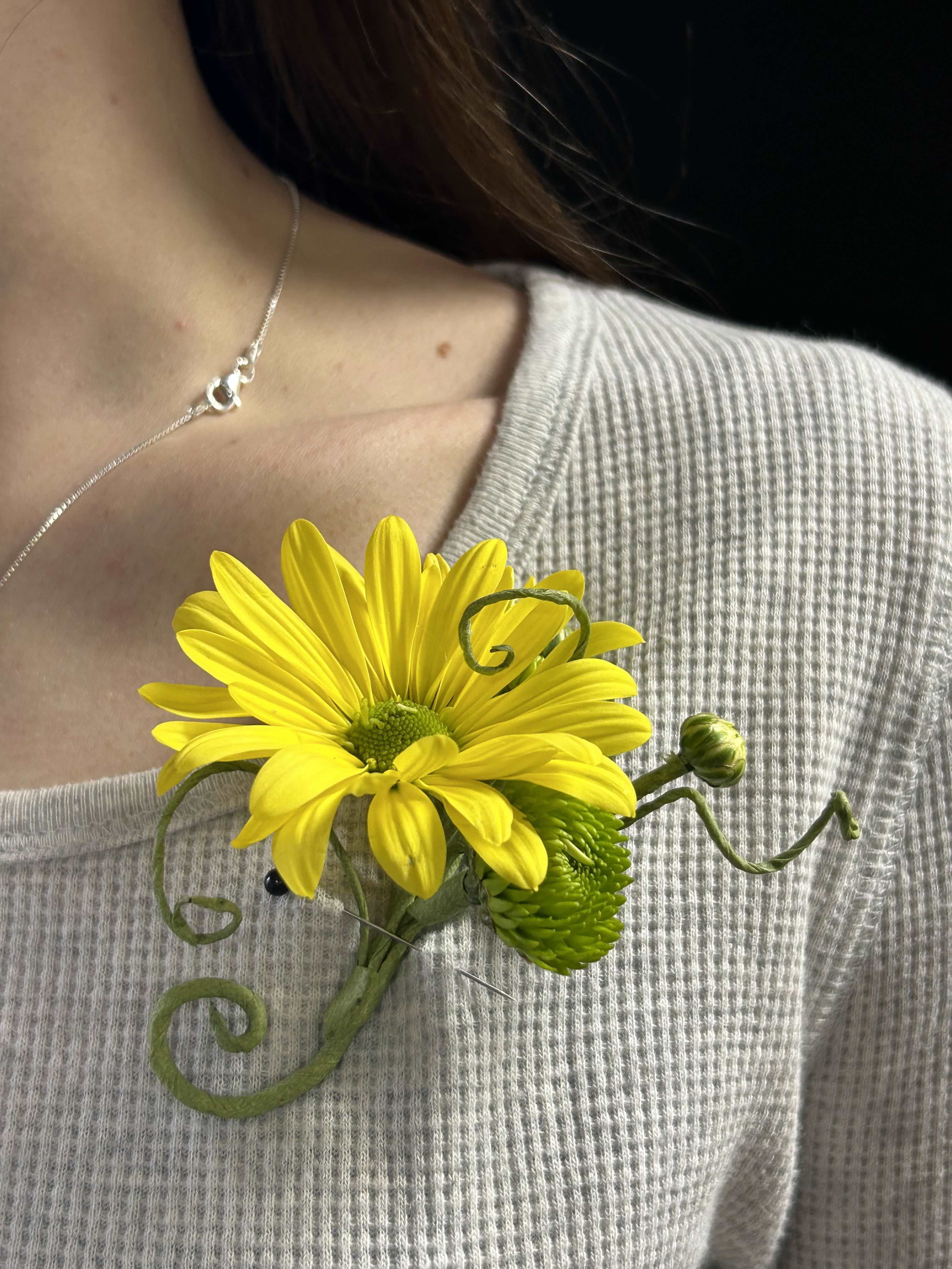 Yellow daisy boutonniere pinned to a sweater