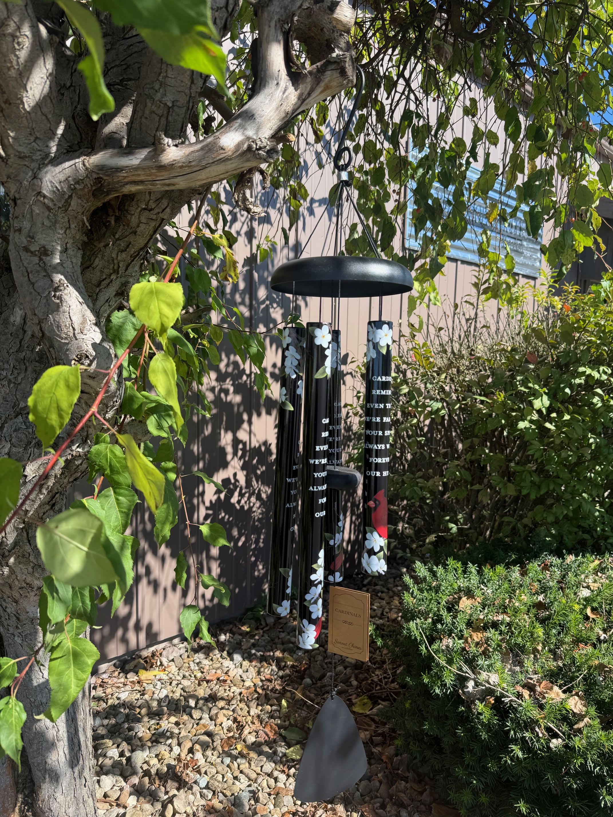 Black memorial wind chime hanging outdoors among trees and shrubs