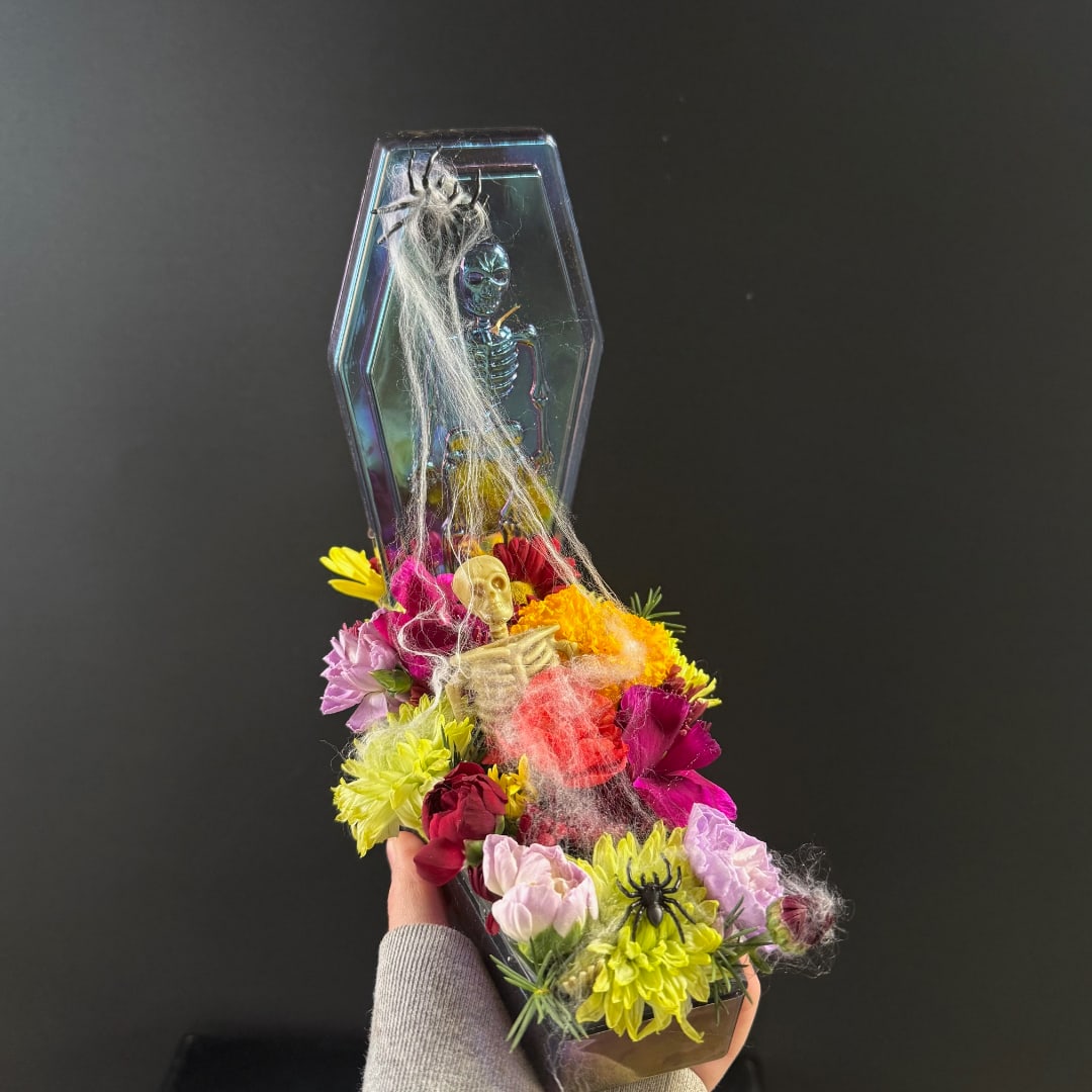 Halloween floral arrangement in a coffin-shaped container with skulls and spider decorations