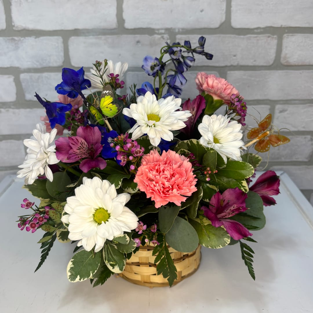 Mixed bouquet in a woven basket with white daisies, pink carnations, and purple blooms