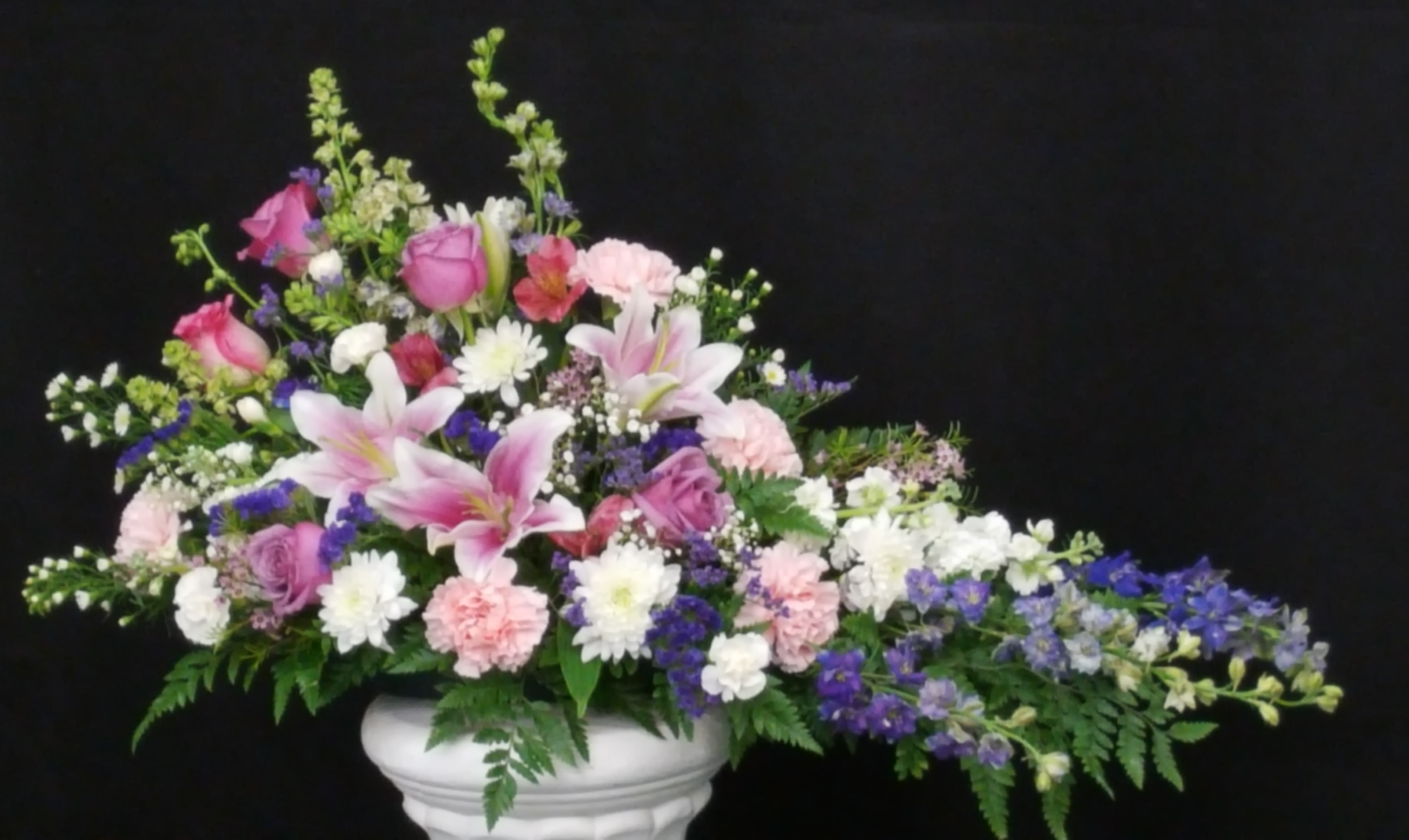 Pink and white mixed flower arrangement in a white pedestal vase