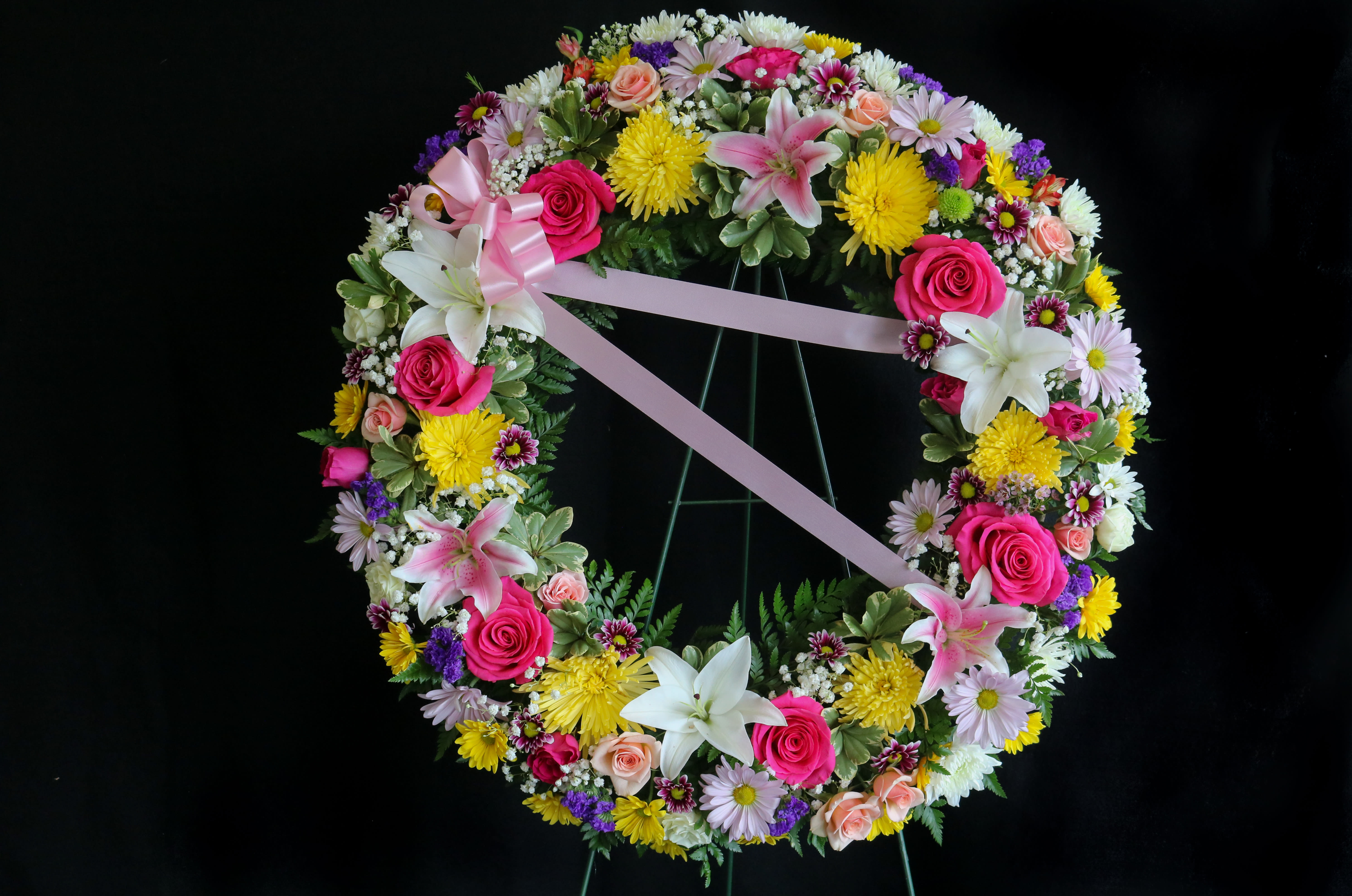 Circular floral wreath with pink ribbon and mixed blooms on a stand