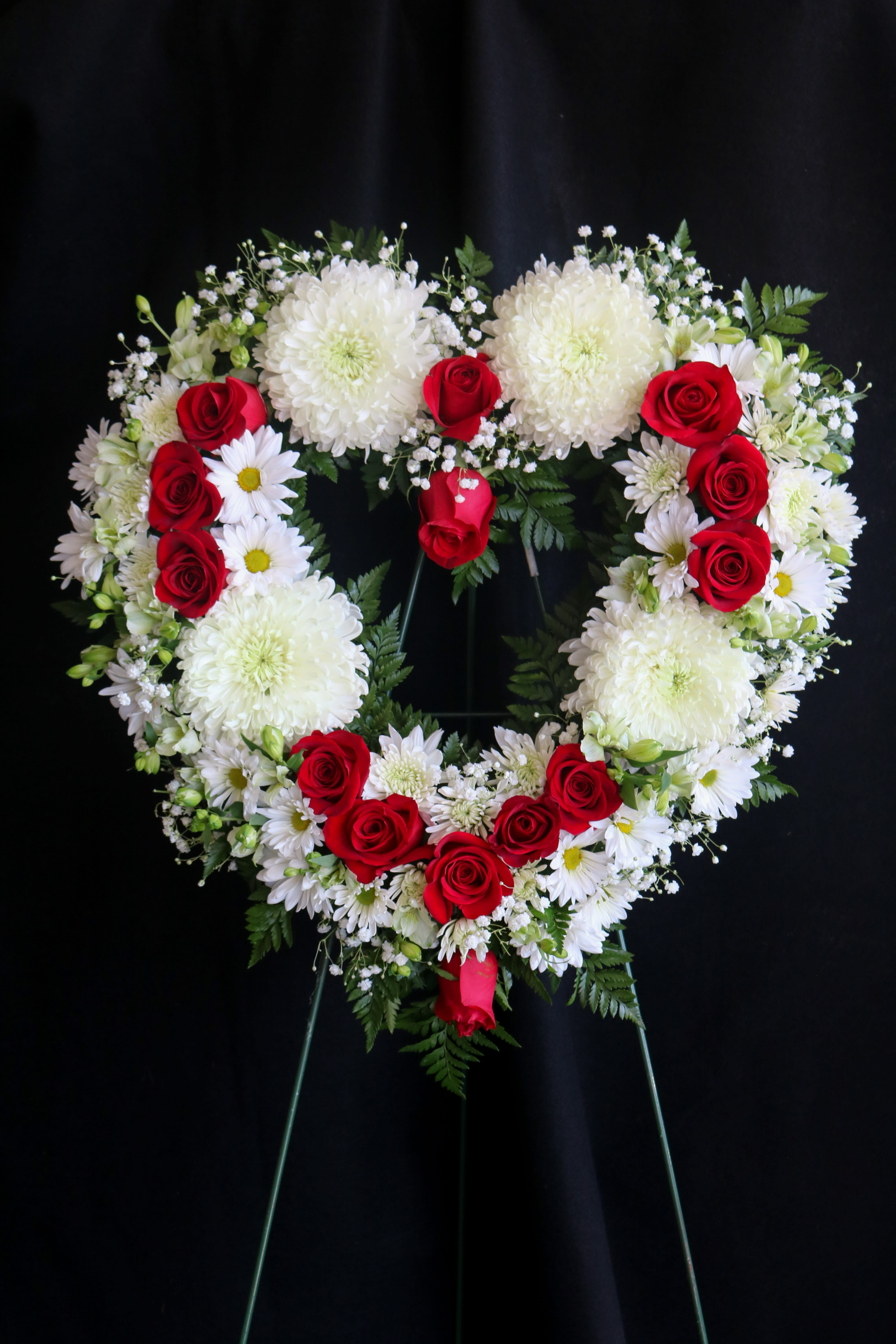 Heart-shaped floral wreath with red roses and white flowers on a stand
