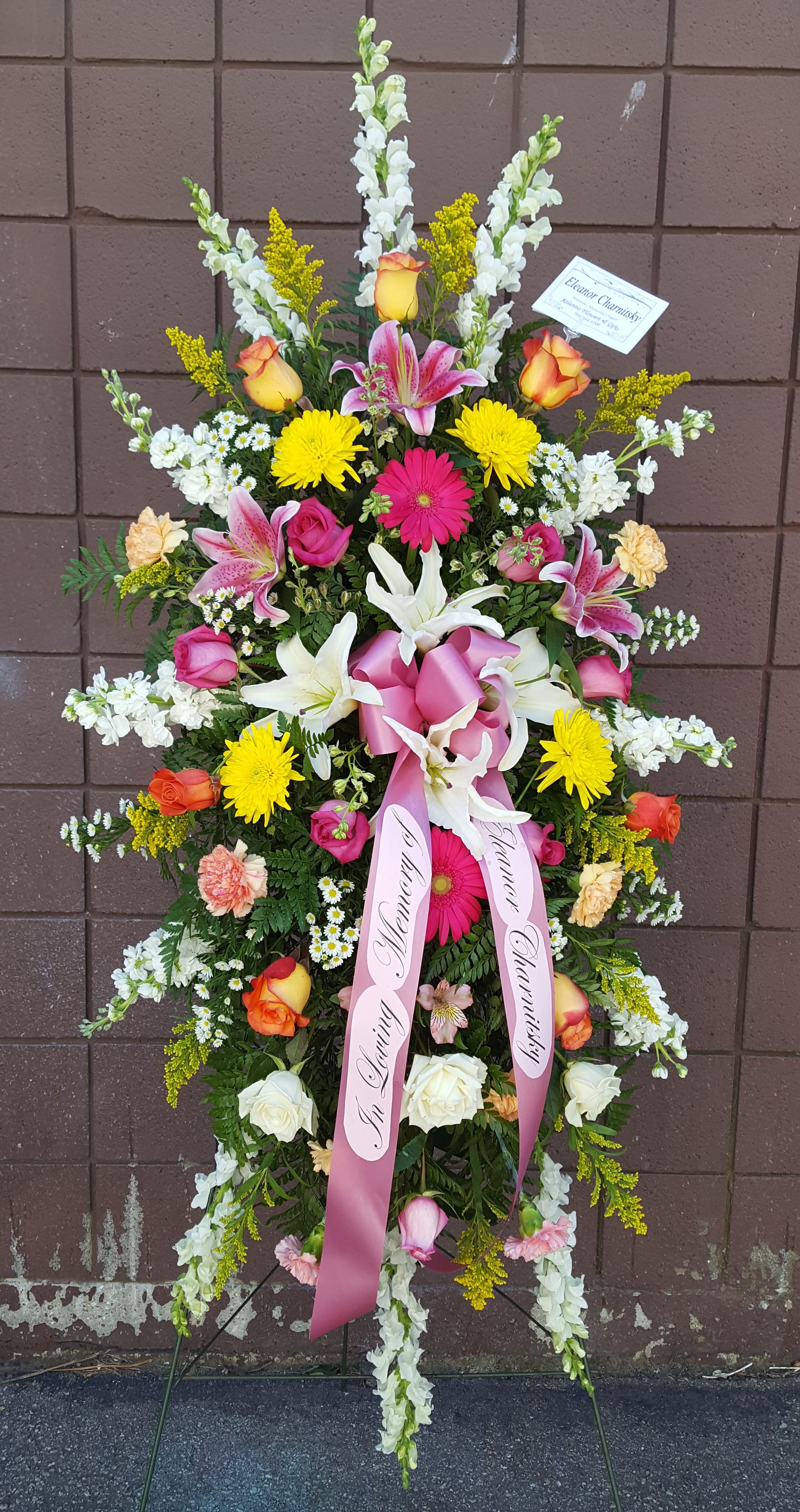 Tall standing spray of mixed flowers with pink ribbons on an easel