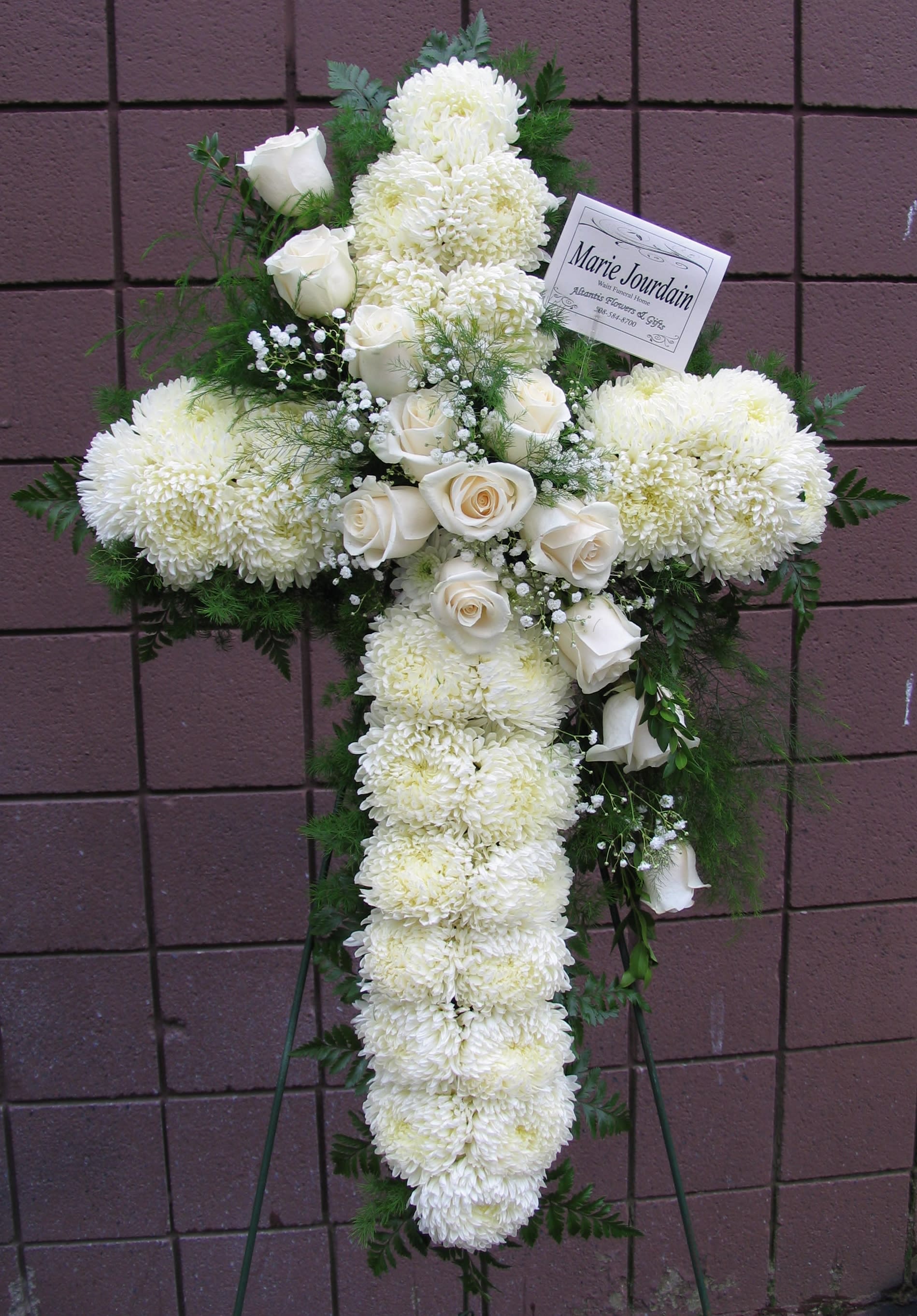 White floral cross on a stand with roses and chrysanthemums