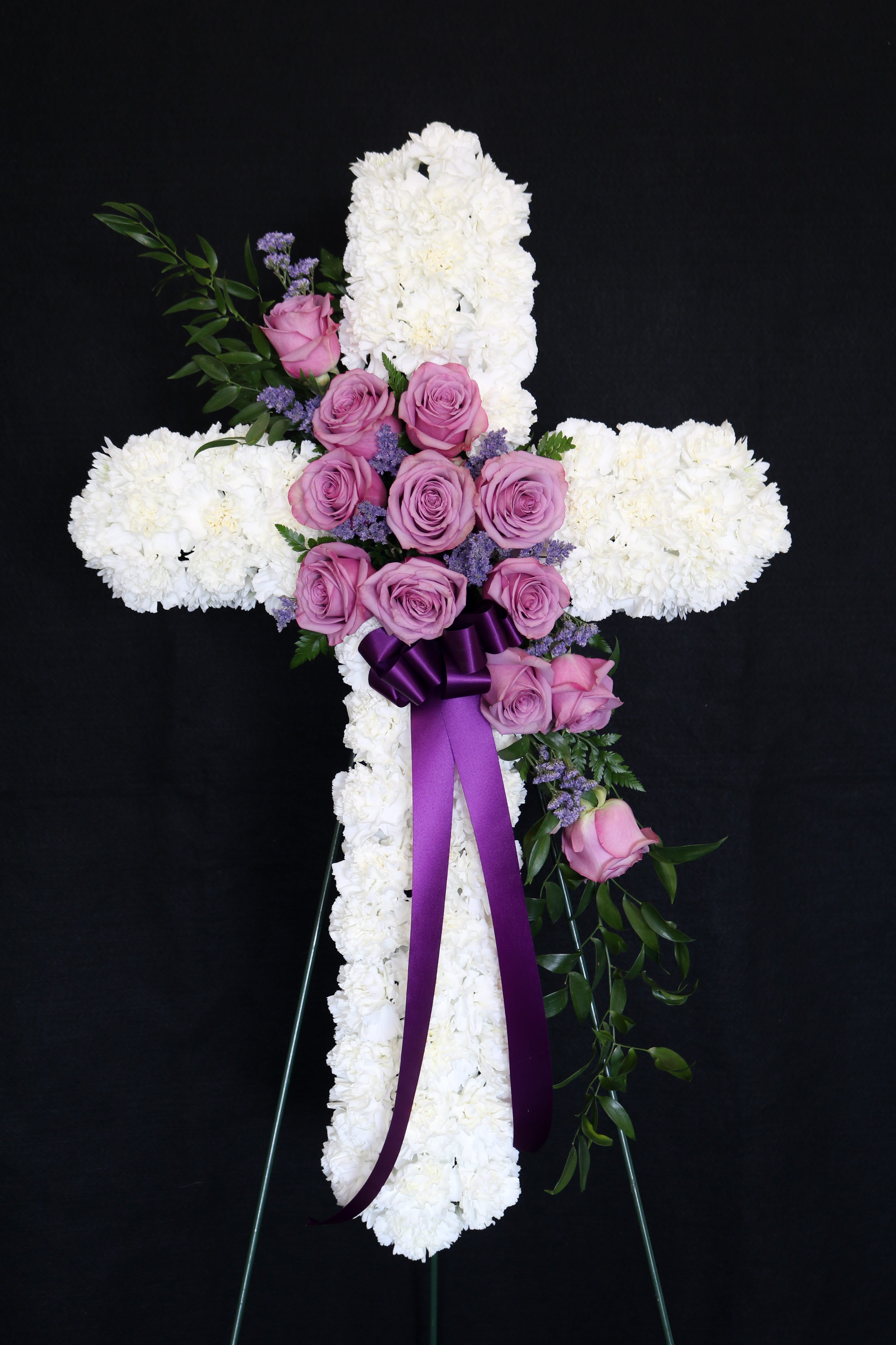 White floral cross with pink roses and a purple ribbon on an easel